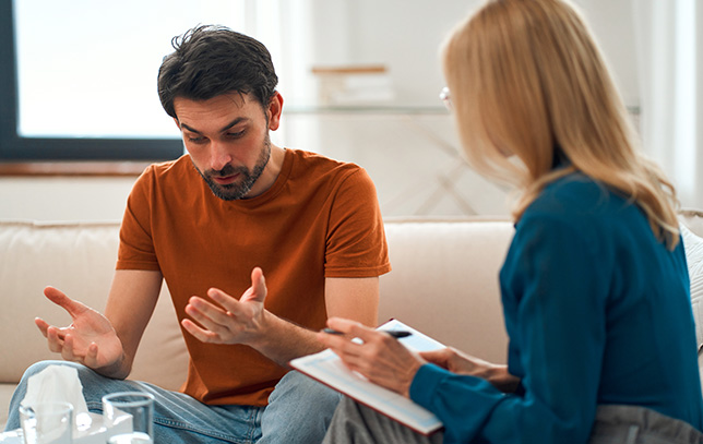 a male patient sitting on a couch chatting with his female psychologist during one on one therapy.